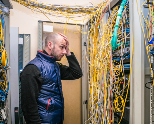 A sad man put his hand to his face at the sight of problems with laying wires in the server room. Incorrect connection of communication equipment in the data center. Wrong work